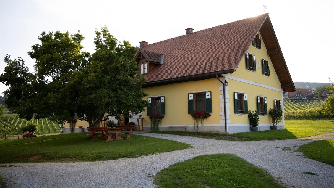 Ein gelbes Haus mit einem roten Dach und grünen Fensterläden, umgeben von Bäumen. Der Garten ist weitläufig und gut gepflegt, ideal für entspannte Tage im Freien. | © TV Südsteiermark - Dominik Feibel