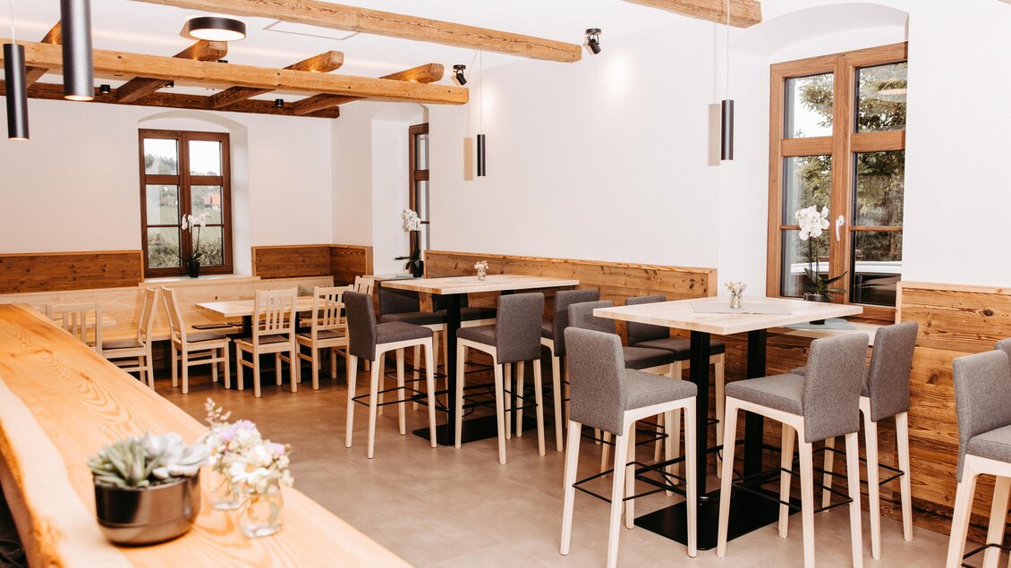 Ein modernes Restaurant mit Holzdekor und gemütlichen Sitzbereichen. Helle Wände und Fenster sorgen für eine freundliche Atmosphäre. | © Trapl - Gasser Benjamin