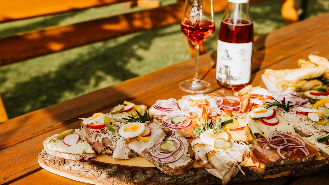Ein schön angerichteter Tisch mit verschiedenen belegten Broten. Im Hintergrund steht ein Glas Roséwein und eine Flasche. | © Trapl - Gasser Benjamin