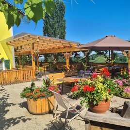 Ein einladender Außenbereich mit bunten Blumen und Holzmöbeln. Der klare Himmel und die Sonnenschirme schaffen eine gemütliche Atmosphäre. | © Weingut Wechtitsch