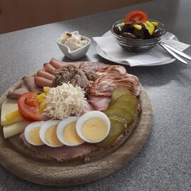 Eine appetitliche Platte mit verschiedenen Wurst- und Käsevariationen, Eiern und Gemüse. Im Hintergrund ein Dessert aus Schokolade und Obst. | © Buschenschank Wiesenhofer