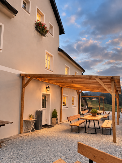 Ein gemütlicher Außenbereich mit Holztischen und Bänken vor einem hellen Gebäude. Die Atmosphäre ist warm und einladend, ideal für entspannte Stunden im Freien. | © Bio Hof Bichler