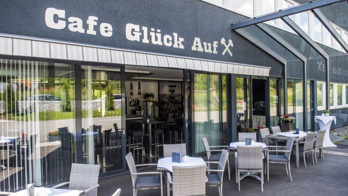 Ein einladendes Café mit dem Namen „Café Glück Auf“. Draußen stehen Tische und Stühle für Gäste. | © Pfripfl Lucas