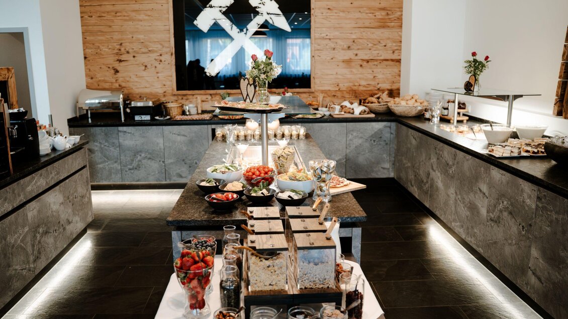 Ein elegantes Buffet mit verschiedenen Speisen und frischen Früchten. Der Raum hat eine moderne, einladende Atmosphäre mit Holz- und Steinelementen. | © Hotel Fohnsdorf  -  Cafè „Glück auf“