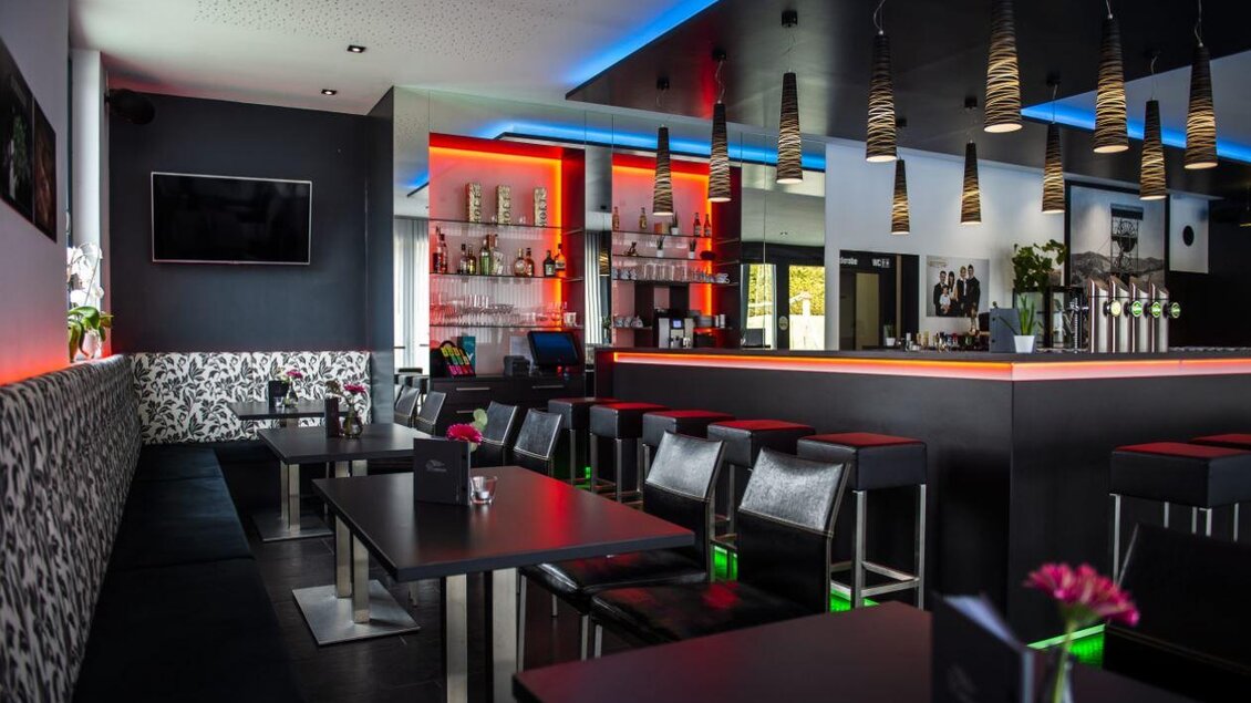 Ein modernes Restaurant mit stilvollen schwarzen Tischen und eleganten Barhockern. Die sanfte Beleuchtung in Rot und Blau schafft eine ansprechende Atmosphäre. | © Pfripfl Lucas