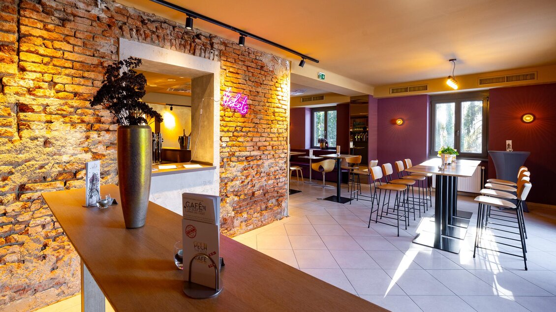Gastraum des Café Marie in Eggersdorf mit Backsteinwand, Holztischen, Barhockern und warmem Licht. | © Harry Schiffer Photodesign