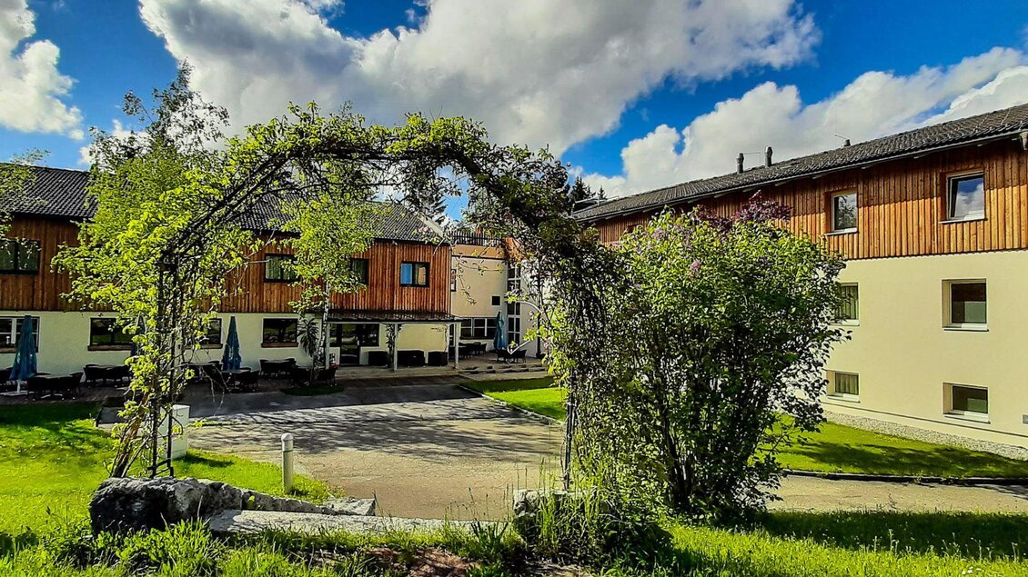 Ein modernes Gebäude mit Holzverkleidung und großen Fenstern. Vor dem Haus befindet sich eine Terrasse mit Tischen und Sonnenschirmen. | © Jufa_Hotel_Bad Aussee_(c) JUFA Hotels