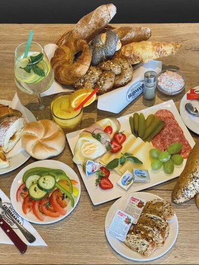 Ein täuschend attraktives Frühstücksarrangement mit verschiedenen Brötchen, Aufschnitt, Käse, frischem Obst und Gemüse. Dazu erfrischende Getränke serviert in bunten Gläsern. | © Bäckerei-Konditorei Hubmann Josef GmbH