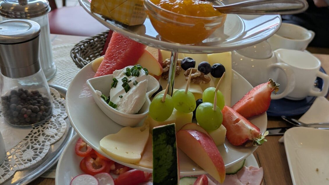 Ein appetitlicher Frühstücksturm mit Wurst, Käse, frischem Obst und Marmelade. Auf mehreren Etagen angerichtet, bietet er eine bunte Auswahl an Leckereien.