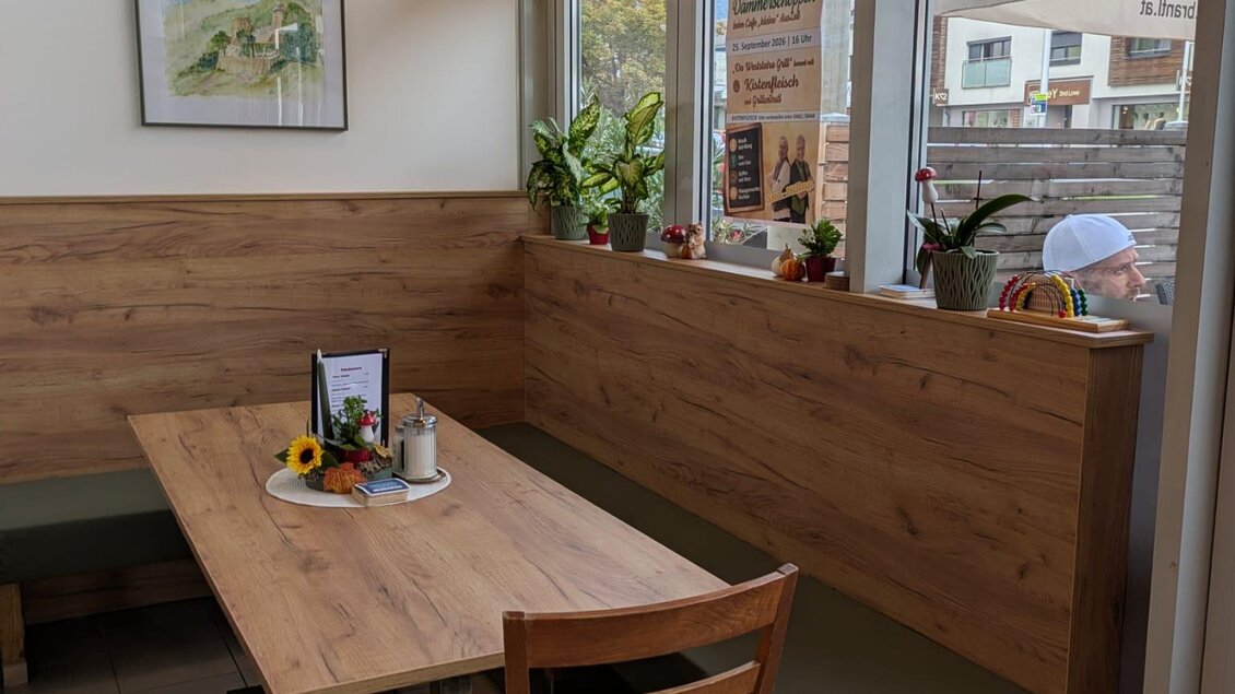 Ein gemütlicher Essbereich mit einem Holztisch und Stühlen. Die Wände sind hell und mit Pflanzen dekoriert, während viel Tageslicht durch die Fenster strömt.