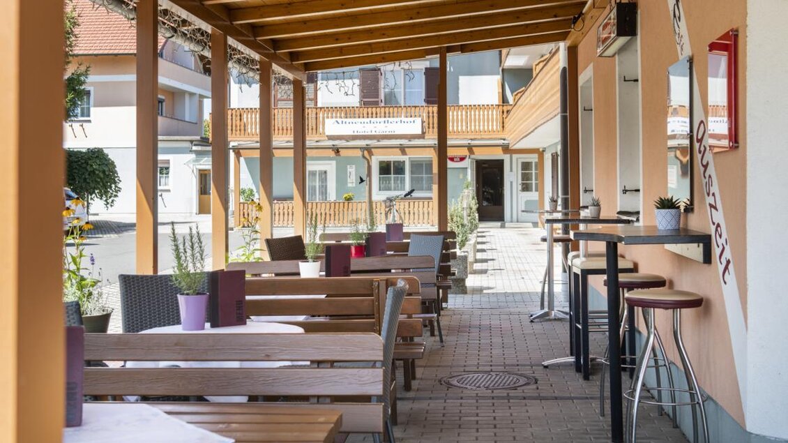 Ein gemütlicher Außenbereich eines Restaurants mit Holztischen und Stühlen. Grüner Pflanzenblick und entspannte Atmosphäre unter einem überdachten Bereich. | © Bachner Hotel BetriebsgesmbH
