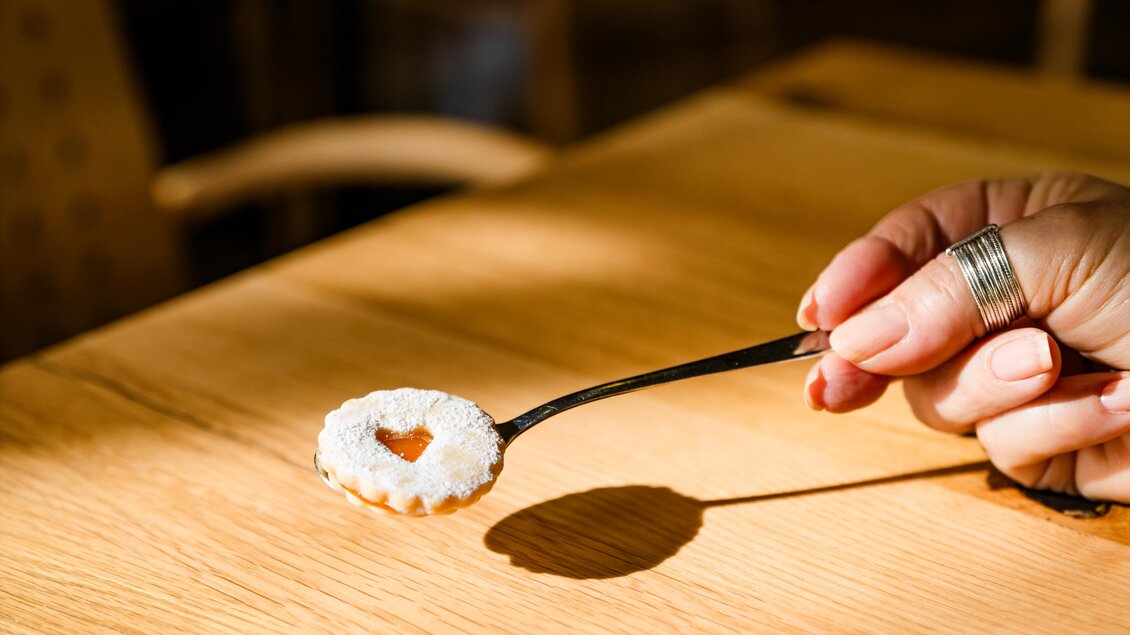 Hand hält Löffel mit Puderzuckergebäck mit Marmeladenfüllung über Holztisch im Café Famoos Unicorn Graz. | © Region Graz - Mias Photoart