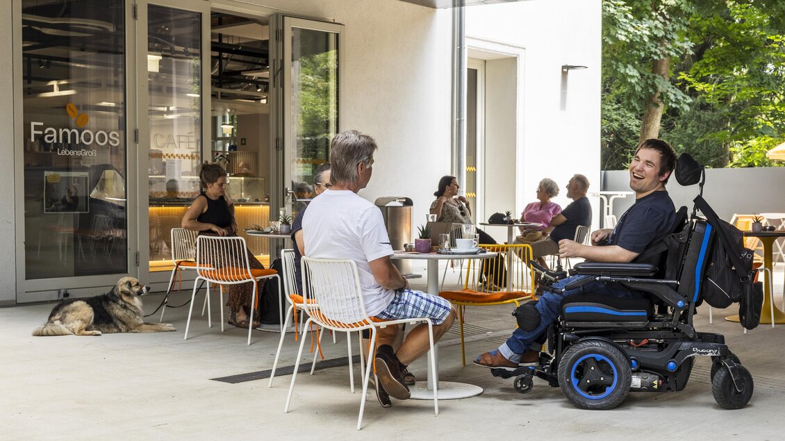 Gäste auf der Terrasse des Café Famoos Graz, darunter ein Mann im Elektrorollstuhl. | © LebensGroß GmbH