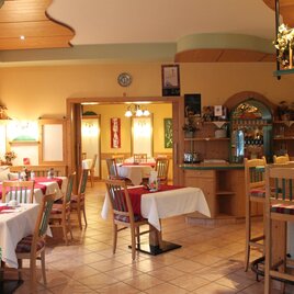 Ein gemütliches Restaurant mit mehreren Tischen und Stühlen. Die Wände sind warm gestaltet und es gibt eine kleine Bar im Hintergrund. | © Café Hotel Garni Thermenoase