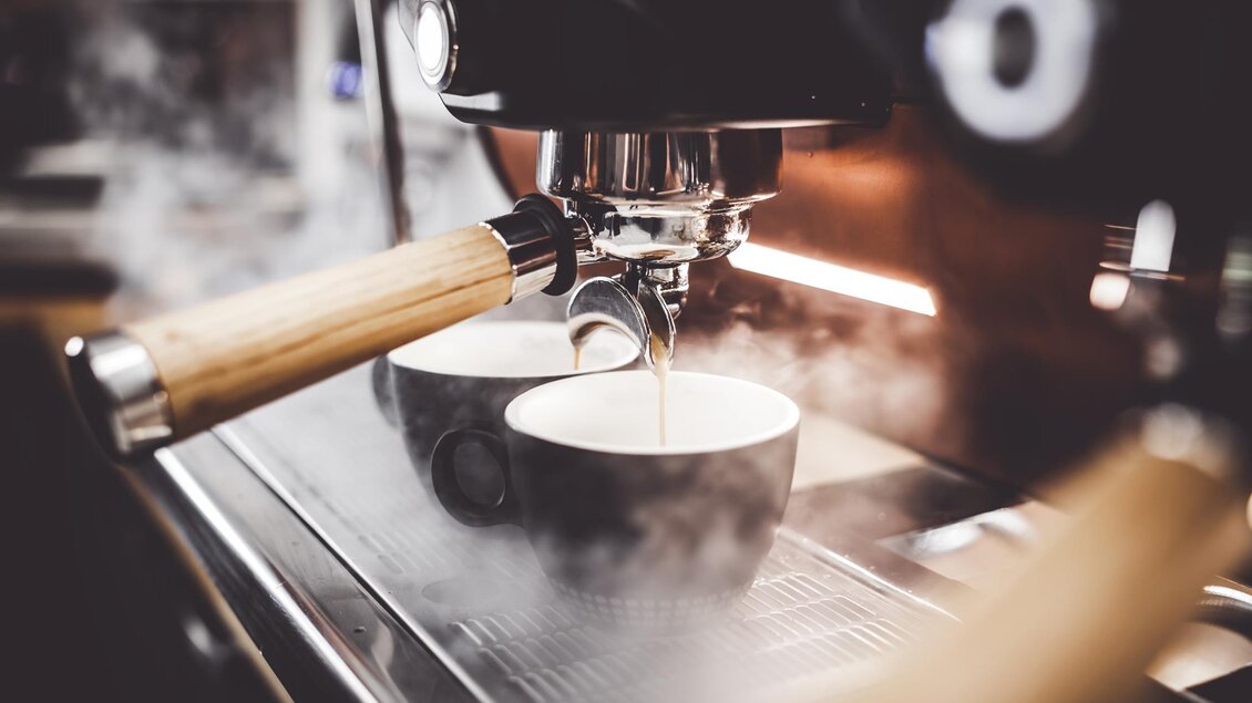 Eine Espresso-Maschine bereitet frischen Kaffee zu. Zwei schwarze Tassen stehen bereit, während Dampf aufsteigt. | © TV Südsteiermark - Adobe Stock