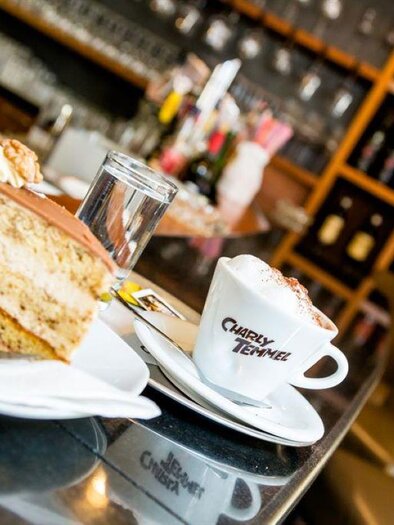 Ein köstliches Stück Kuchen auf einem Teller, daneben eine Tasse Kaffee. Im Hintergrund ist eine elegante Bar mit Regalen voller Getränke zu sehen. | © Stephan Friesinger