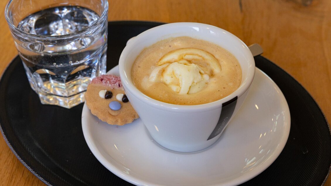 Tasse Kaffee mit Milchschaum und Glas Wasser auf Tablett in der Café-Konditorei Famoos in Mooskirchen.  | © LebensGroß GmbH