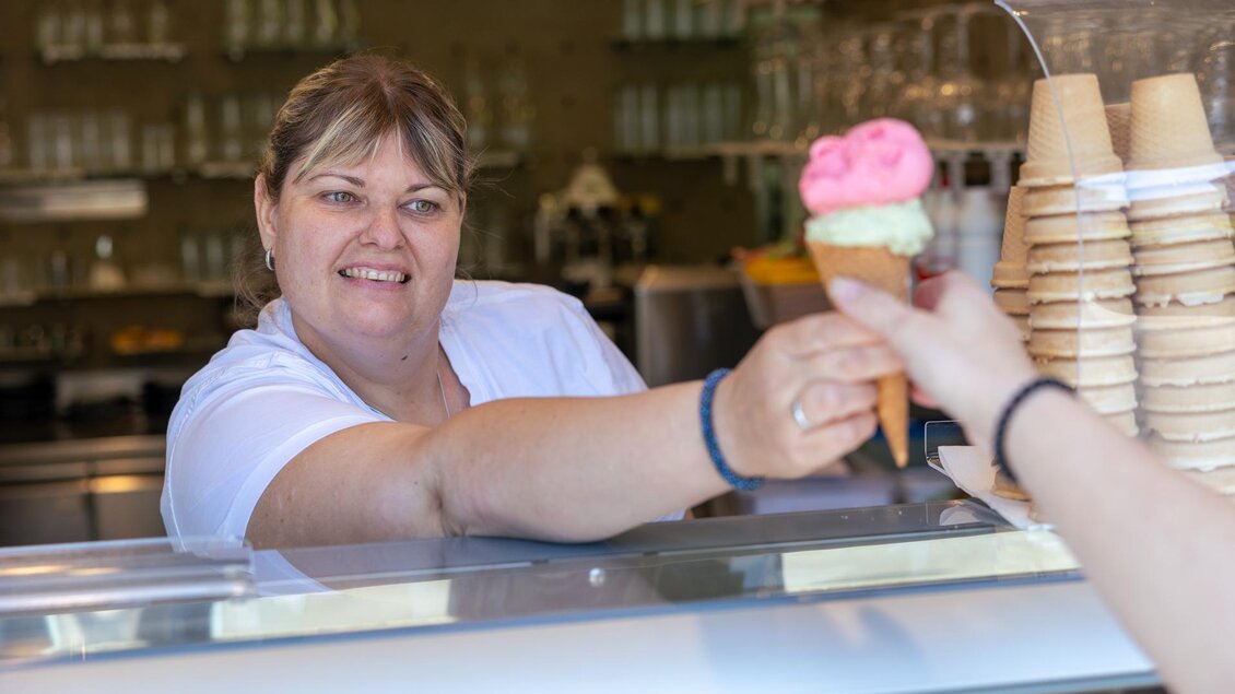 Mitarbeiterin reicht eine Kugel Eis in der Café-Konditorei Famoos in Mooskirchen an einen Gast. | © LebensGroß GmbH