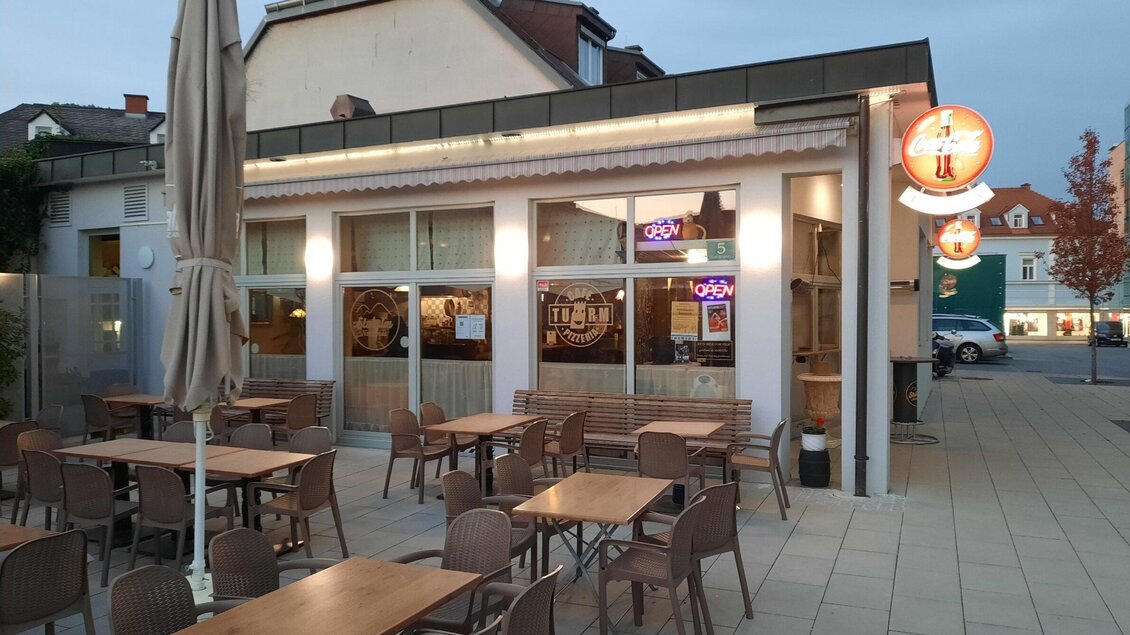 Außenansicht des Café-Pizzeria Turm mit Gastgarten und Sitzplätzen in Köflach bei Abendstimmung. | © Mara