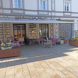 Ein gemütliches Café mit Außenterrasse und bunten Blumen in blühenden Kästen. Die Fassade des Gebäudes ist historisch gestaltet. | © Bäckerei Freydl