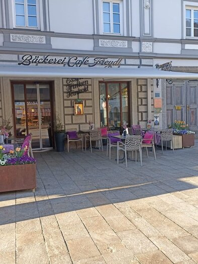 Ein gemütliches Café mit Außenterrasse und bunten Blumen in blühenden Kästen. Die Fassade des Gebäudes ist historisch gestaltet. | © Bäckerei Freydl