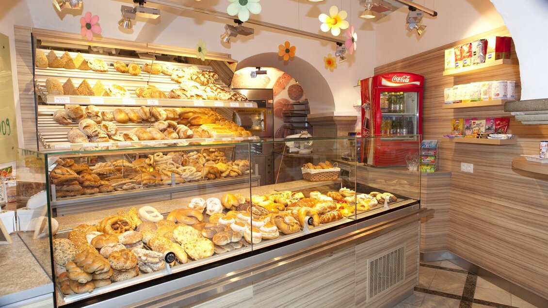 Eine Bäckerei mit einer großen Auswahl an frischen Backwaren. Im Hintergrund sind ein Getränkekühlschrank und dekorative Blumen zu sehen. | © Bäckerei Freydl