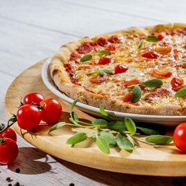 Eine frisch gebackene Pizza mit Käse, Tomaten und frischem Basilikum. Daneben liegen rote Kirschtomaten auf einem Holzbrett. | © Pixabay