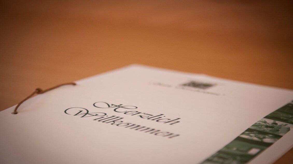 Ein elegantes Willkommensschild auf einem Tisch. Der Text "Herzlich Willkommen" ist schön gestaltet und lädt Gäste ein. | © GH Mauthner Kirchenwirt