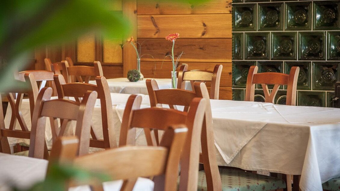 Ein einladendes Restaurant mit Holztischen und Stühlen. Die Tische sind weiß gedeckt und eine Blume verleiht eine freundliche Atmosphäre. | © GH Kirchenwirt Wies