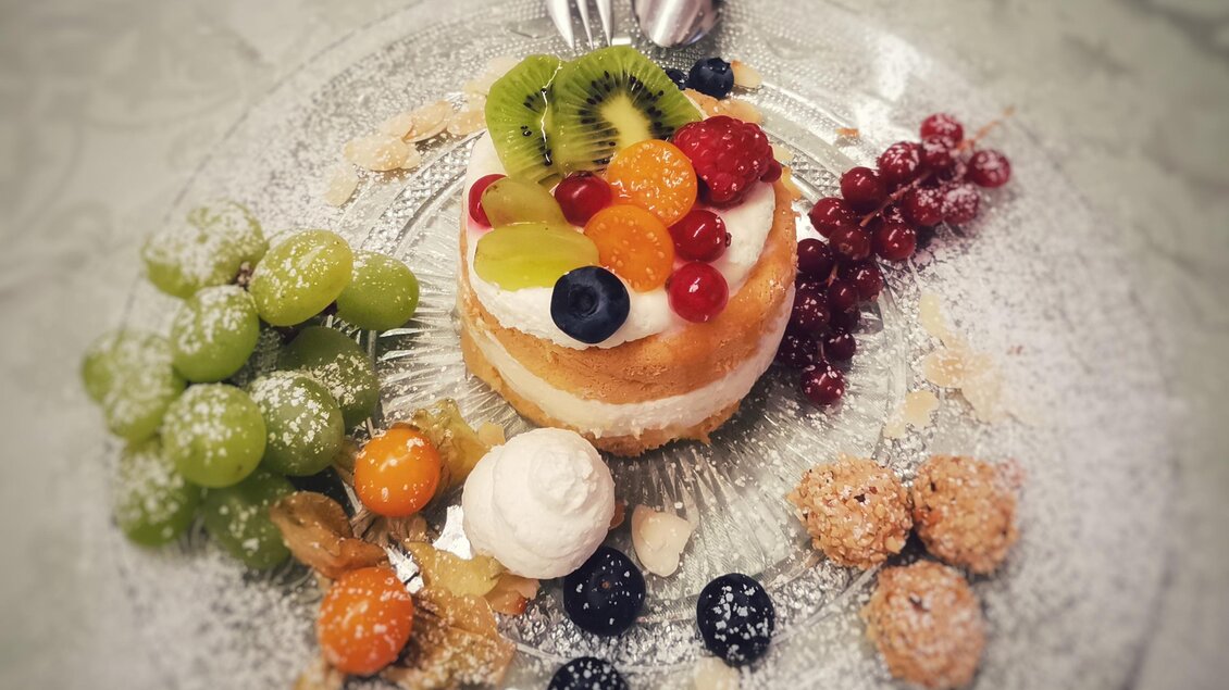 Ein schöner Dessertteller mit einer fruchtigen Torte und verschiedenen Früchten. Die Torte ist dekoriert mit Kiwi, Himbeeren und Heidelbeeren.