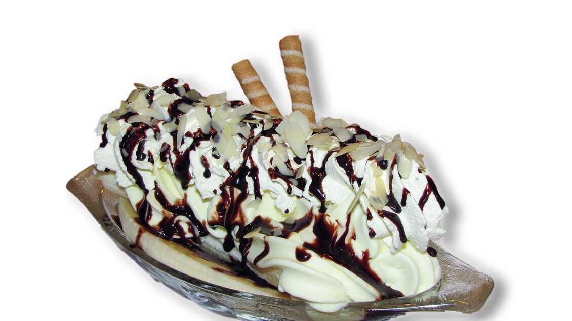 Ein köstliches Eisdessert in einer Glasschale. Es ist mit Sahne, Schokoladensauce und Waffelröllchen garniert.