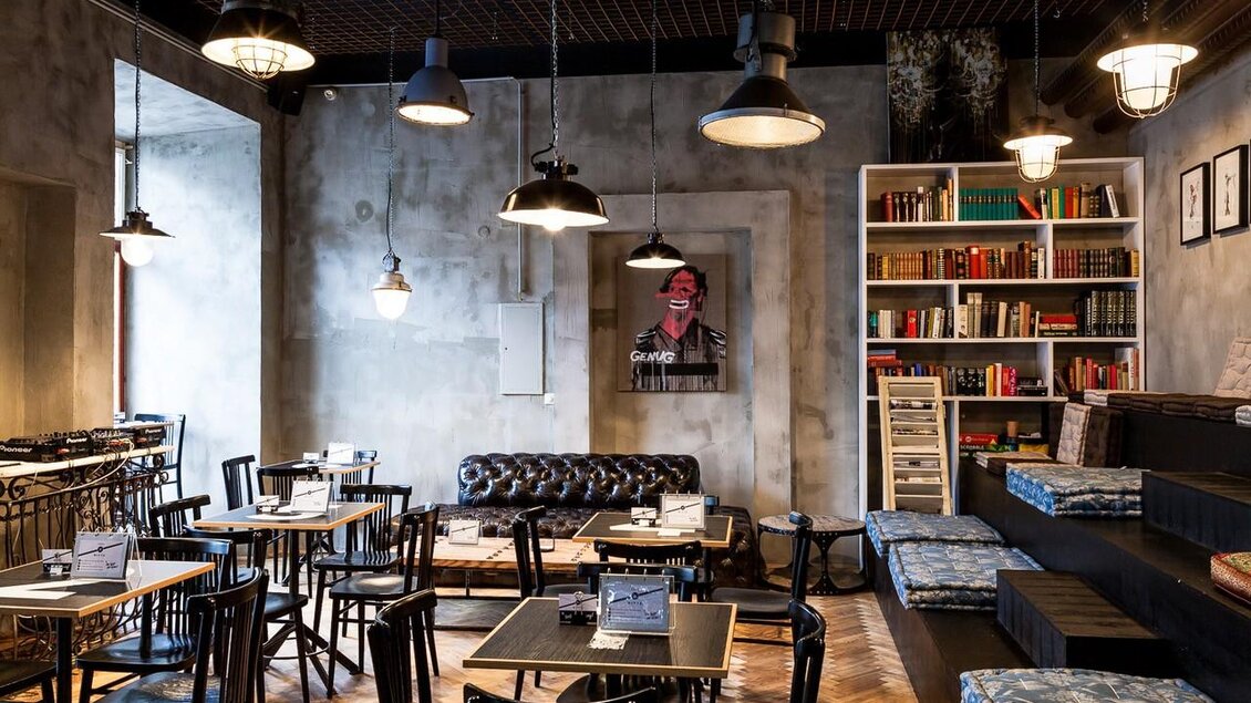 Innenbereich im Cafe Mitte Graz mit Tischen, Stühlen, Ledersofa, Bücherregal und Sitzstufen im industriellen Stil. | © Cafe Mitte