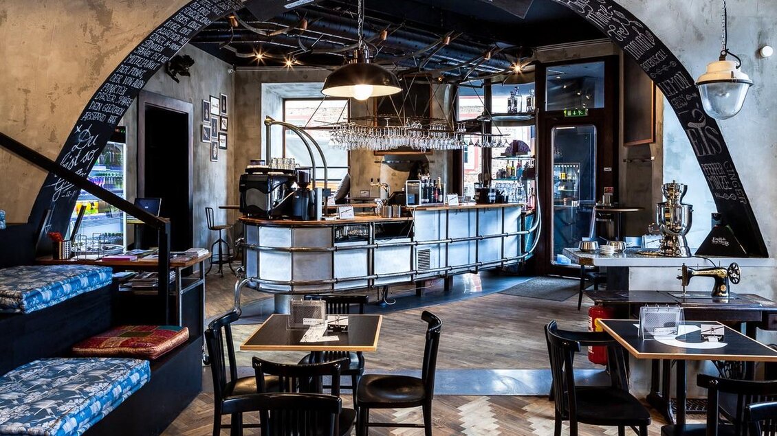 Bar im Cafe Mitte Graz mit Theke, Gläsern, Sitzplätzen und schwarzem Bogen mit Beschriftung im industriellen Stil.  | © Cafe Mitte