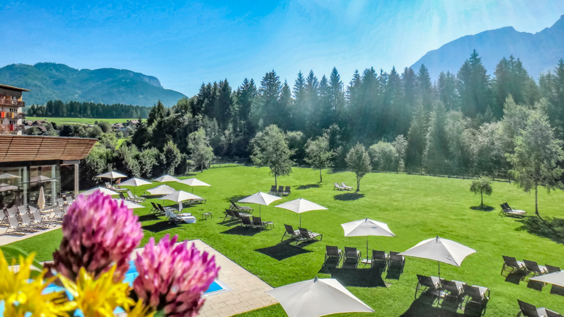<p><p>Die grüne Gartenanlage des Aldiana Clubhotel mit Sonnenliegen und Sonnenschirmen. Im Hintergrund sind die Berge des Ausseerlandes mit dem Grimming auf der rechten Seite und einem strahlend blauen Himmel zu sehen.</p></p> | © Aldiana Salzkammergut