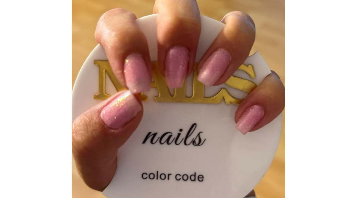 Eine Hand mit perfekt manikürten Nägeln in sanften Farben hält das Logo von Color Code Nails fest.  | © Eszter David