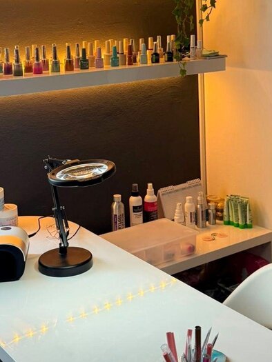 Das Color Code Nagelstudio innen mit einem eleganten Tisch auf dem eine Vergrößerungslupe und verschiedene Nagellacke stehen. Im Hintergrund sind Pflegeprodukte und eine gemütliche Beleuchtung zu sehen.</p> | © Eszter David