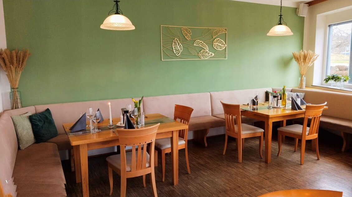 Ein gemütliches Restaurant mit Holztischen und Stühlen. Die Wände sind in sanften Grüntönen gestrichen und mit Pflanzen-Dekorationselementen versehen. | © Lisa Pilko