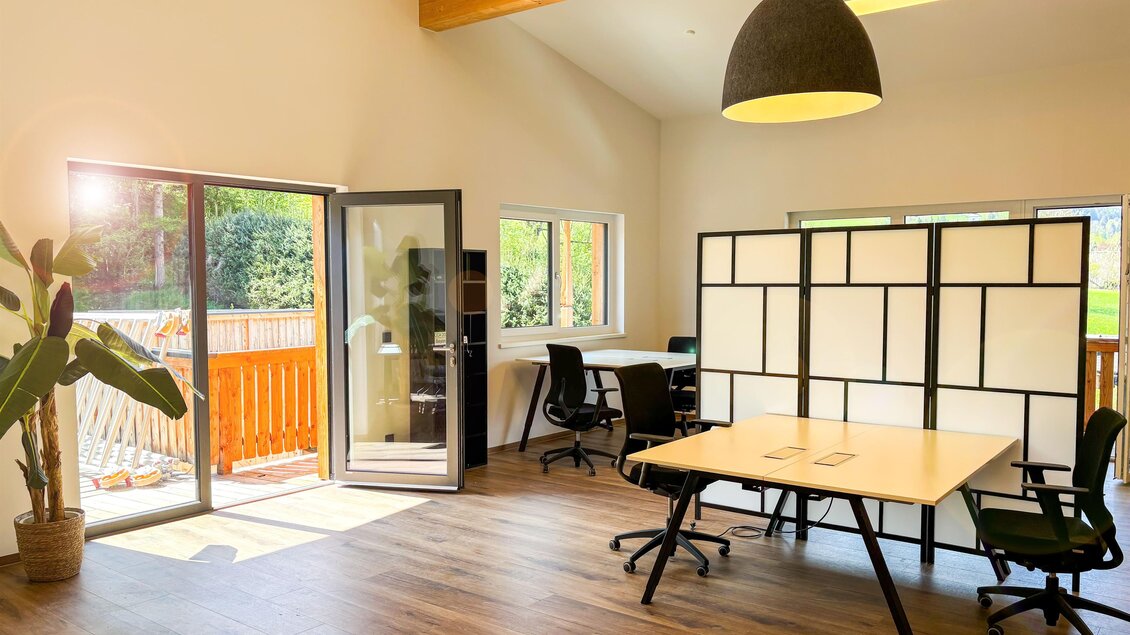Ein helles, modernes Büro mit großen Fenstern und einem offenen Raumkonzept. Es gibt einen Schreibtisch, Stühle und Pflanzen, die eine angenehme Atmosphäre schaffen. | © Coworking Space