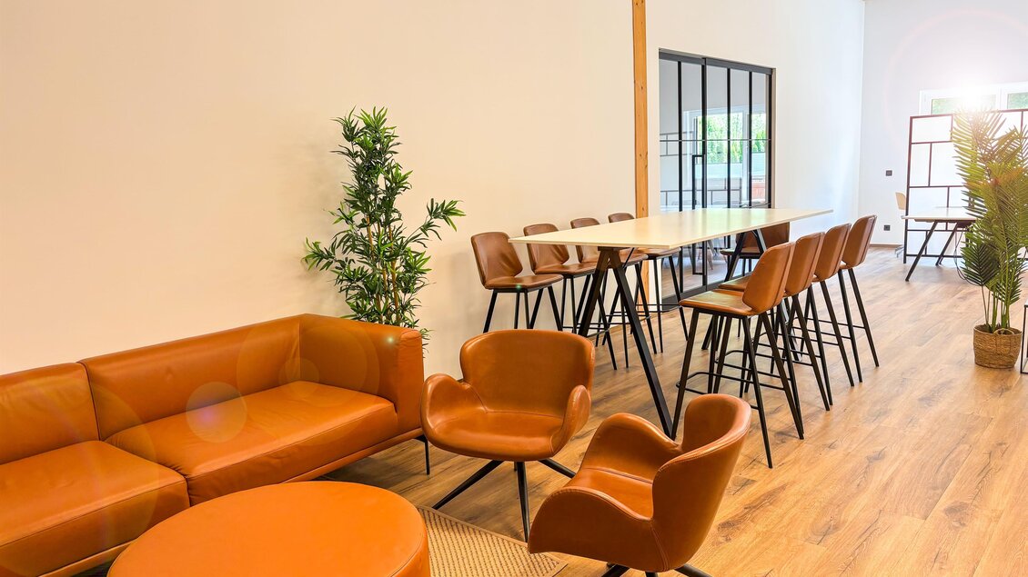 Ein modernes und gemütliches Büro mit orangefarbenen Möbeln. Es gibt einen langen Tisch und ein paar Pflanzen, die für eine angenehme Atmosphäre sorgen. | © Coworking Space