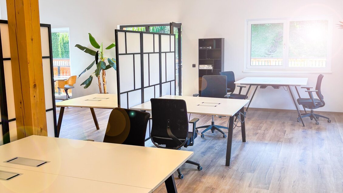 Ein modernes Büro mit hellen Wänden und Holzdecke. Es gibt mehrere Schreibtische und Pflanzen, die eine angenehme Arbeitsatmosphäre schaffen. | © Coworking Space