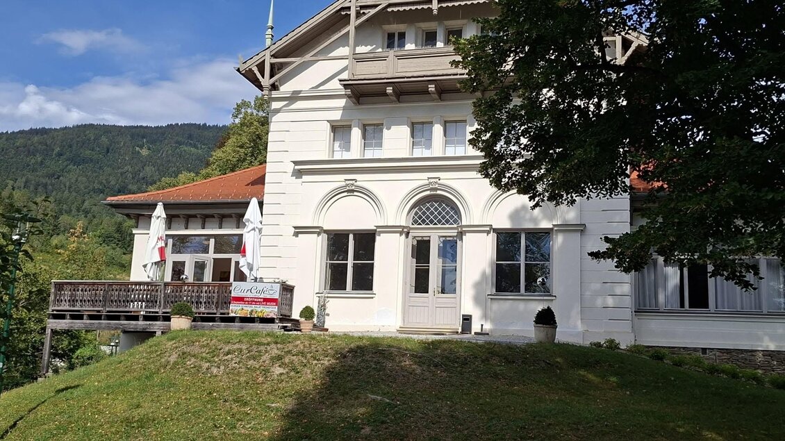 Weißes Gebäude des CurCafés in St. Radegund mit Terrasse, Bäumen und bewaldetem Hügel im Hintergrund. | © Bernhard Glauninger