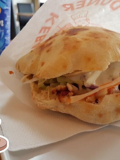 Ein frisch zubereitetes Dönerbrot mit Fleisch, Salat und Sauce. Neben dem Döner steht eine Flasche Ayran. | © Döner Kebap Haus Sevindi