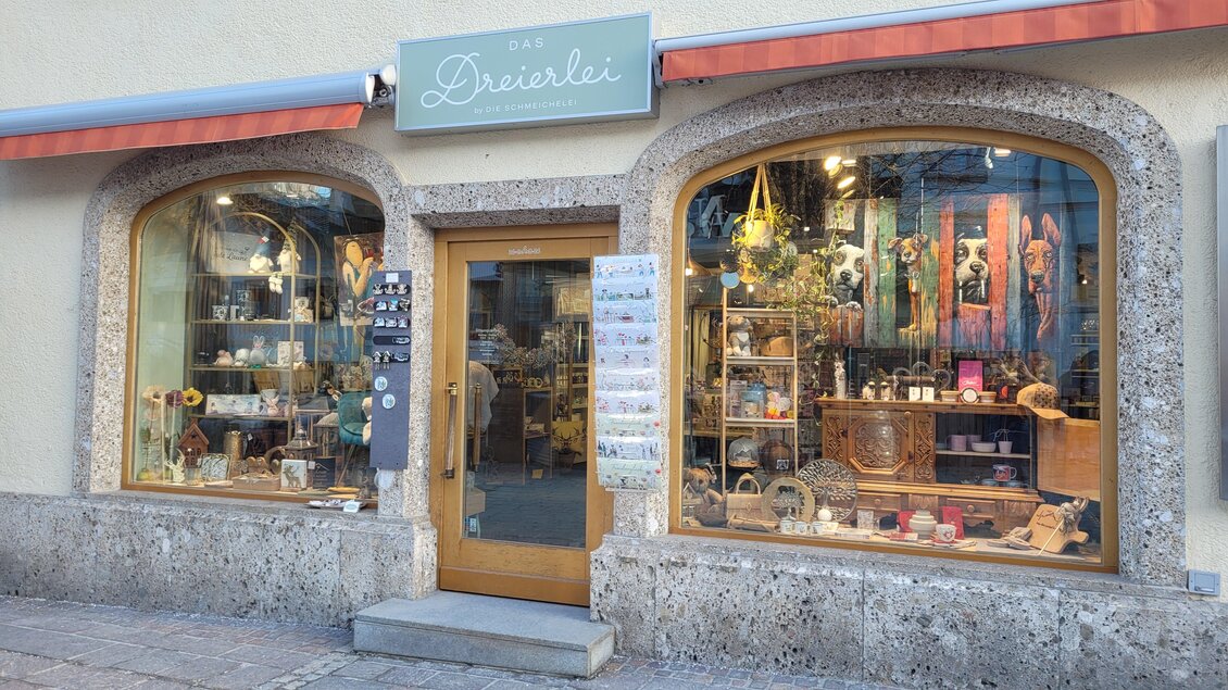 Ein einladendes Geschäft mit Schaufenster, das eine Vielzahl von handgefertigten Artikeln zeigt. Im Vordergrund sind Regale mit dekorativen Gegenständen und Geschenken zu sehen.