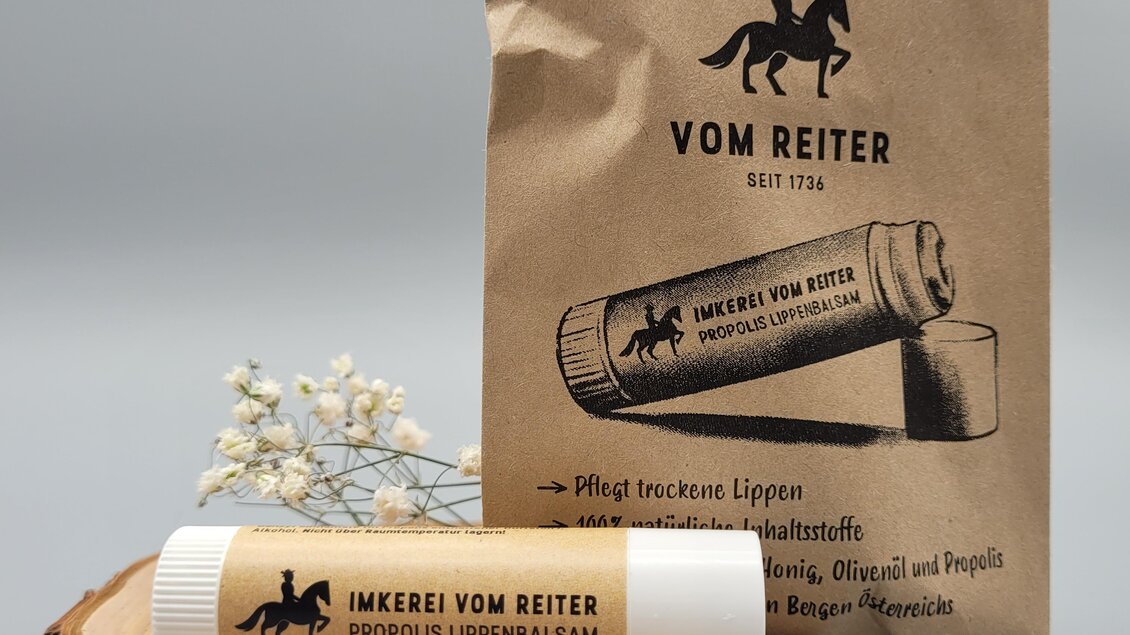 Ein Lippenbalsam auf einer Holzscheibe, umgeben von natürlicher Dekoration. Die Verpackung ist schlicht und trägt das Logo "VOM REITER".