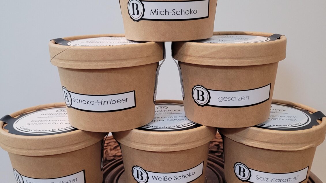 Sechs Eislöffelbehälter aus Pappe stehen übereinander. Jeder Behälter hat ein Etikett mit der Geschmacksrichtung.