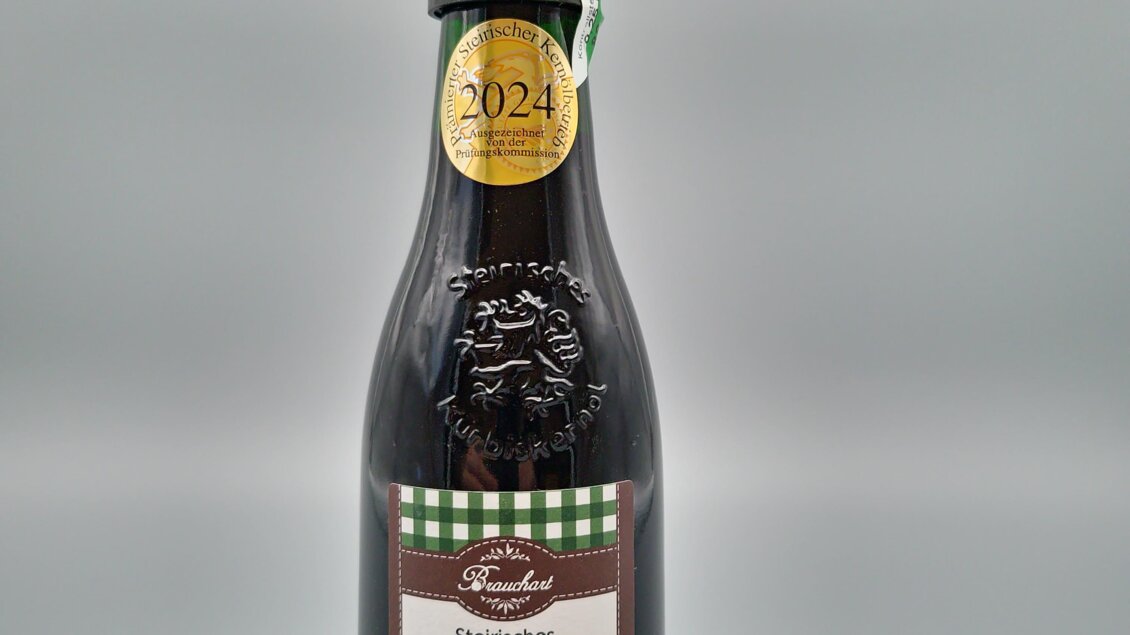 Eine Flasche steirisches Kürbiskernöl steht auf einem Holzuntersetzer. Das Etikett zeigt verschiedene Informationen über das Produkt.