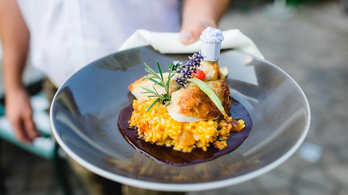 Ein schön angerichteter Teller mit Risotto und gebratenem Fisch. Das Gericht ist mit frischen Kräutern und Gemüse dekoriert. | © A.M.J. Hotel KG