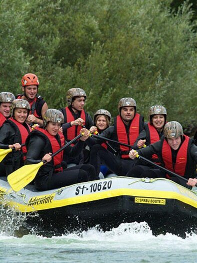 A group of people is paddling in a raft on a wild river. They are wearing life jackets and helmets while having fun. | © Dachstein Tauern Adventure