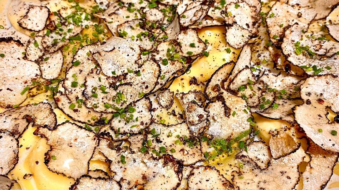 Ein Gericht mit einer cremigen Sauce, bedeckt mit dünn geschnittenen Trüffeln und frischen Kräutern. Die Kombination verspricht einen luxuriösen Geschmack. | © Sabine Marschnig