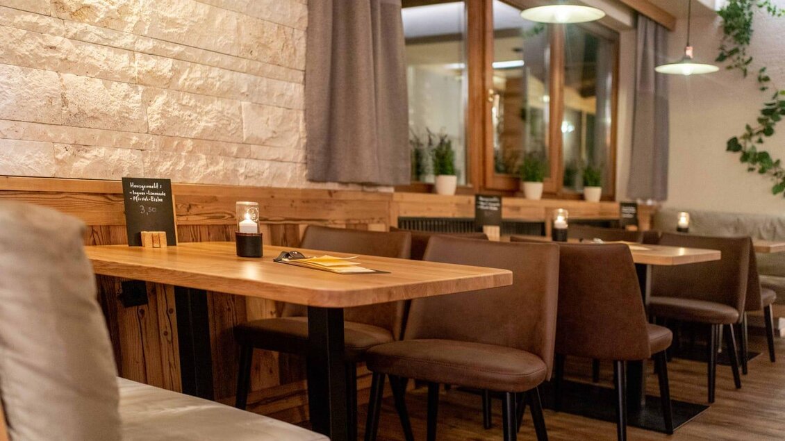 Ein gemütliches Restaurant mit Holzstühlen und Tischen. Sanfte Beleuchtung und Pflanzen sorgen für eine einladende Atmosphäre. | © Maurer